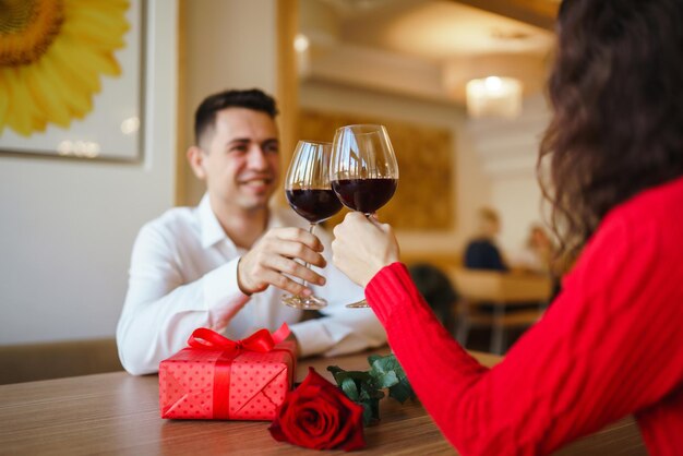 Couple clink glasses with red wine Lovers give each other gifts Lovely romantic dinner