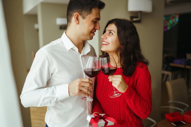 Couple clink glasses with red wine Lovers give each other gifts Lovely romantic dinner