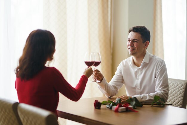 Couple clink glasses with red wine Lovers give each other gifts Lovely romantic dinner