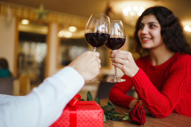 Couple clink glasses with red wine Lovers give each other gifts Lovely romantic dinner