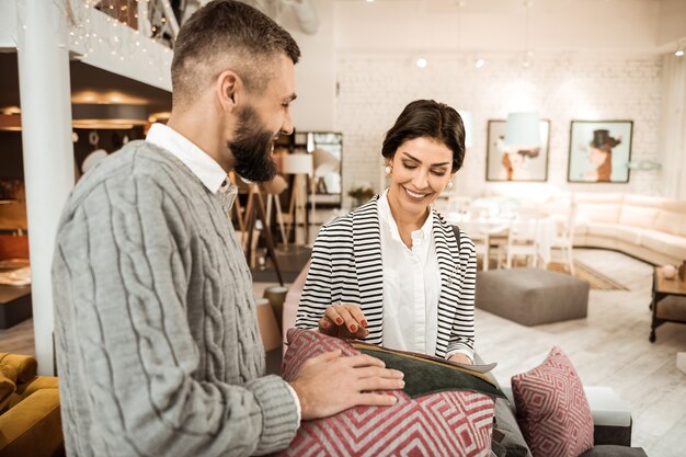 Couple comparing colors. Smiling tidy woman being interested in process of home shopping with her supportive husband