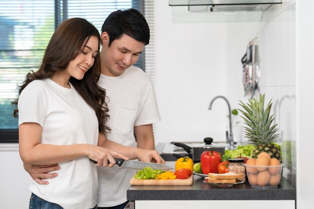 Coppia che taglia le verdure per preparare cibo sano in cucina a casa l'uomo sta abbracciando la donna