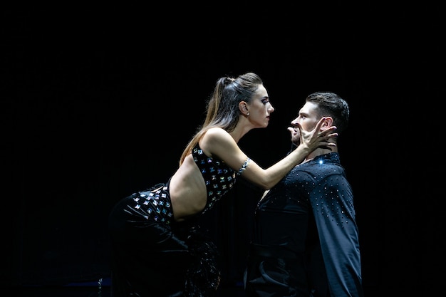 Couple of dancers performing on isolated black. Muscular handsome man and attractive blonde woman