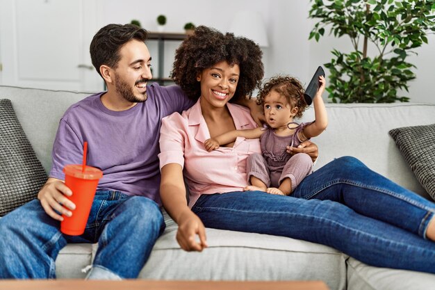 Couple and daughter watching movie sitting on sofa at home