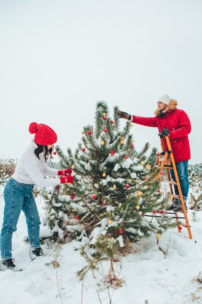 屋外でクリスマスツリーを飾るカップルは、冬の屋外で雪が降った