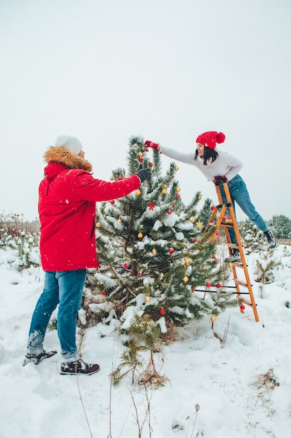 Couple decorating christmas tree outdoors snowed winter outdoors