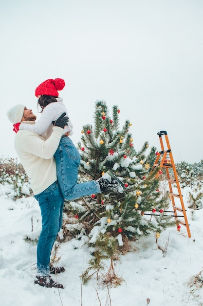 屋外でクリスマスツリーを飾るカップルは、冬の屋外で雪が降った
