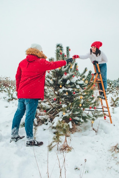 Couple decorating christmas tree outdoors snowed winter outdoors