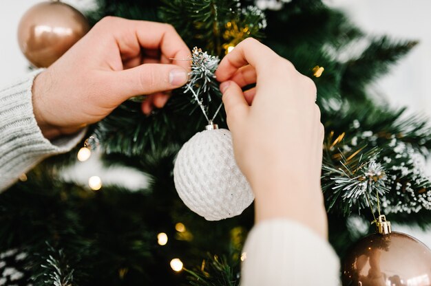 Couple decorating a Christmas tree with a ball Man and woman decorate the tree indoors