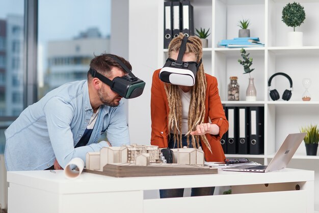 Couple of designers or engineers analyse mock-up of future residential area using ar goggles in architectural bureau.