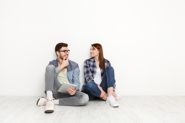 Couple discuss something, sitting on floor with tablet on white background at new apartment