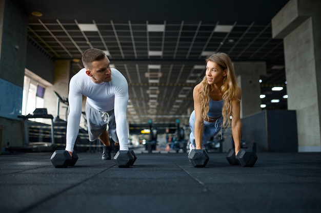 Couple doing push-ups with dumbbells in gym