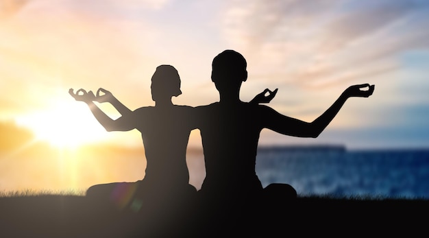 couple doing yoga in lotus pose over sunset