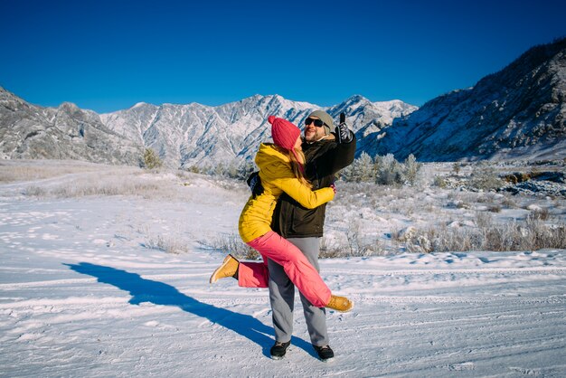 Couple dressed in bright clothing hugs against snow mountains and blue sky