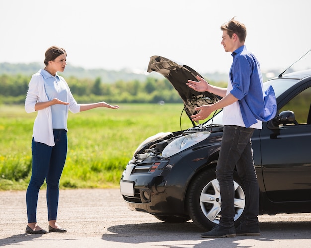 壊れた車の近くでCoupleを持つカジュアルな服装のカップル。