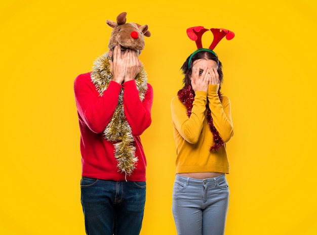 Couple dressed up for the christmas holidays covering eyes by hands and looking through th