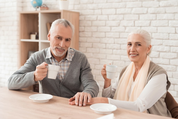 Couple drinking coffee, holding hands together at home.