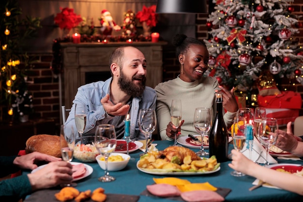 Пара пьет игристое вино на рождественском праздничном ужине, предлагает тосты, держит бокал на рождественском домашнем застолье. Молодая семья празднует зимний праздник, ест традиционные блюда на новогодней вечеринке