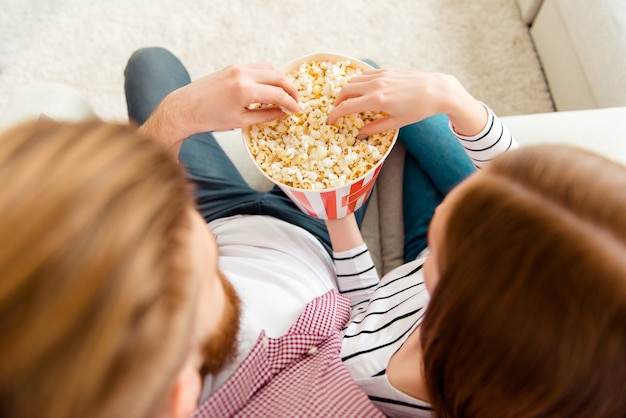 自宅のソファでポップコーンを食べてテレビを見ているカップル