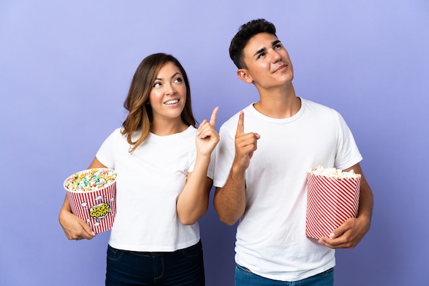 Couple eating popcorn while watching a movie on purple pointing with the index finger a great idea