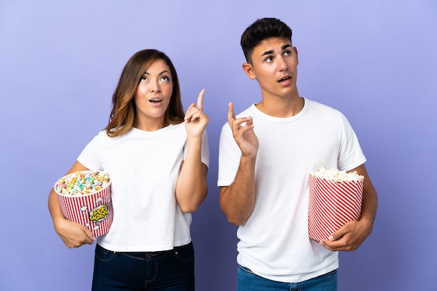 Couple eating popcorn while watching a movie on purple thinking an idea pointing the finger up