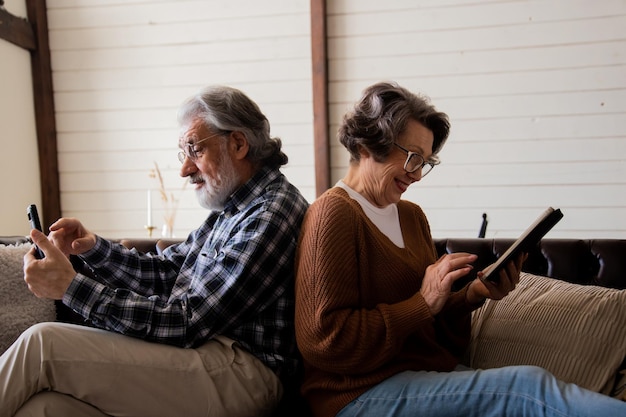 몇 명의 노인 남녀가 가제트를 적극적으로 사용합니다. 성숙한 남편과 아내는 소파에 앉아 있습니다.