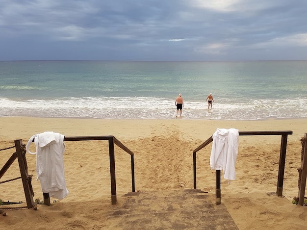 Photo a couple of elderly people go to swim in the sea in the morning against the backdrop of a gloomy sky