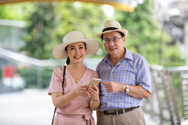 couple elderly with hat standing at outdoor look on mobile phone.