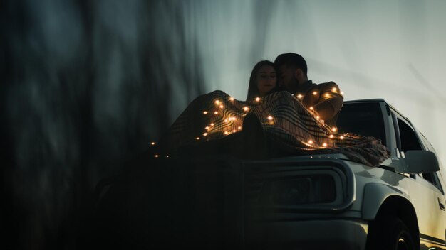Foto coppia che si abbraccia mentre è seduta in macchina con le luci a stringa al crepuscolo