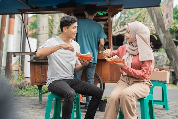 カップルはインドネシアの屋台の食べ物の売り手から購入したチキンサテを食べるのを楽しんでいます