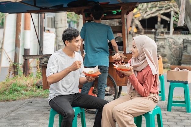 カップルはインドネシアの屋台の食べ物の売り手から購入したチキンサテを食べるのを楽しんでいます