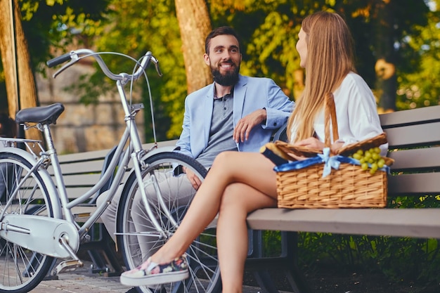 A couple enjoy a picnic on a bench in a park.