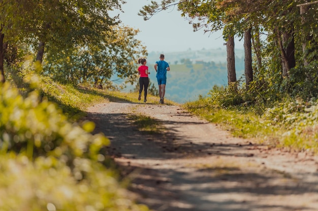 Couple enjoying in a healthy lifestyle while jogging on a country road through the beautiful sunny forest, exercise and fitness concept.