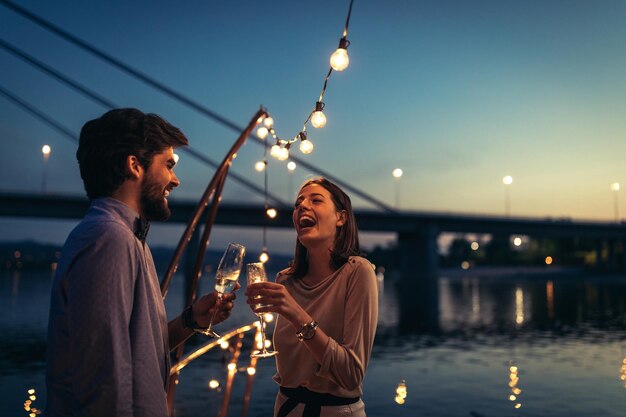couple enjoying sunset at the party by the river holding beer bottles and laughing