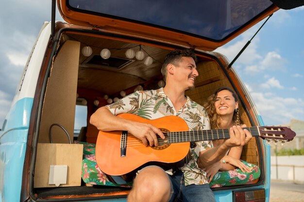 Couple enjoying while playing the guitar in a road trip with a retro van