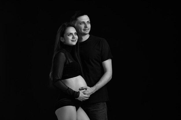 Couple expecting baby and hugging on black background