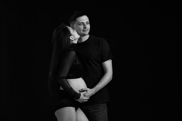 Couple expecting baby and hugging on black background