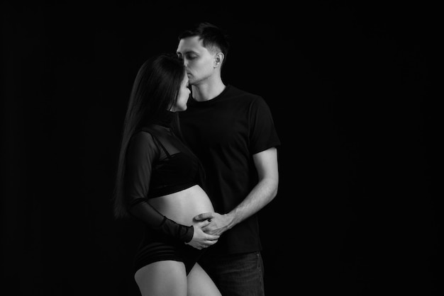 Couple expecting baby and hugging on black background