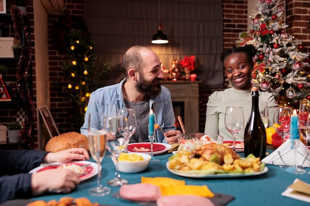 Couple at family christmas holiday celebration, happy friends eating, drinking sparkling wine at festive served dinner table. Man and woman enjoying xmas dishes at home party