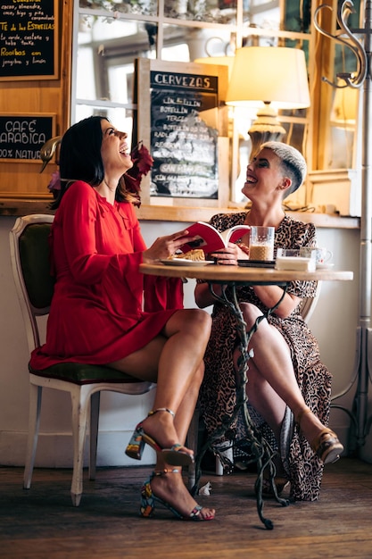 A couple of female friends laugh and read a book in a modern bar