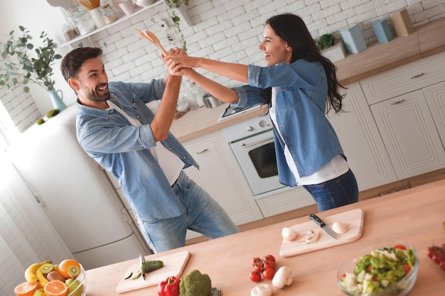 Couple fighting on spatulas in the kitchen while preparing dinner