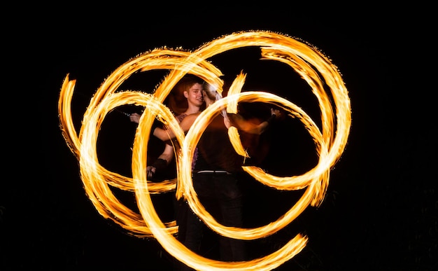 Foto coppia di artisti del fuoco creano schemi infuocati che fanno girare pois ardenti nell'oscurità notturna all'aperto, art.