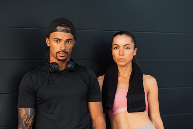 Couple in fitness wear relaxing at a black wall
