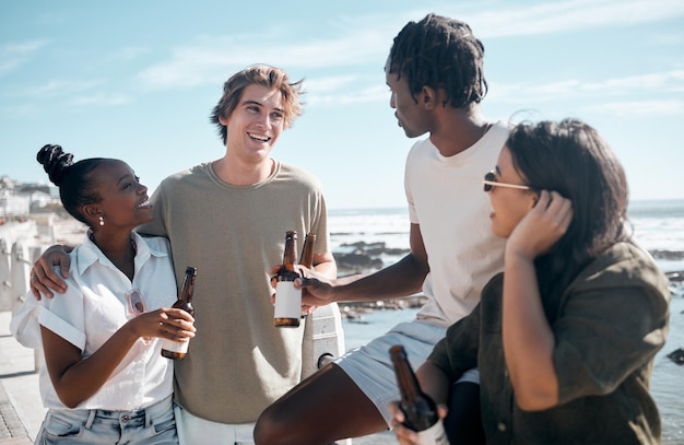 Photo couple of friends talking or drinking beer by beach ocean or sea in holiday vacation summer travel or social gathering smile happy or bonding people and alcohol drinks for diversity celebration