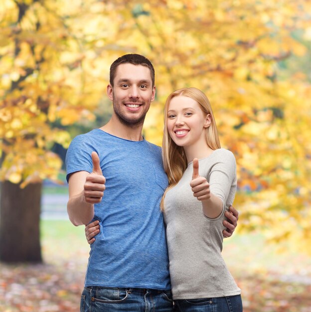 Concetto di coppia, gesto e famiglia - coppia sorridente che mostra i pollici in su