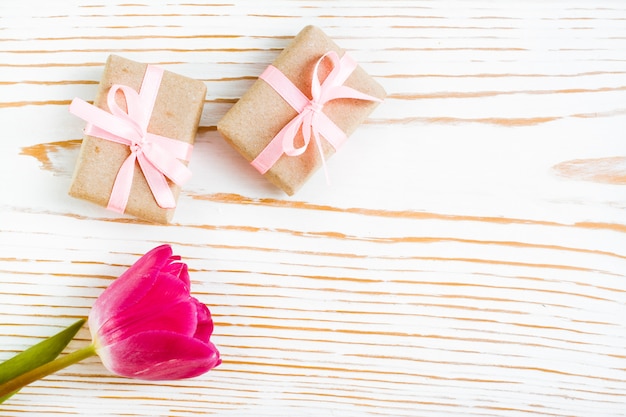 Пара подарков, завернутые с розовой лентой и тюльпан на белой древесине, вид сверху