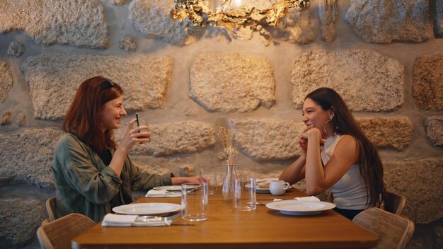 Couple girls mates laughing in cafeteria drinking beverages under lamp light