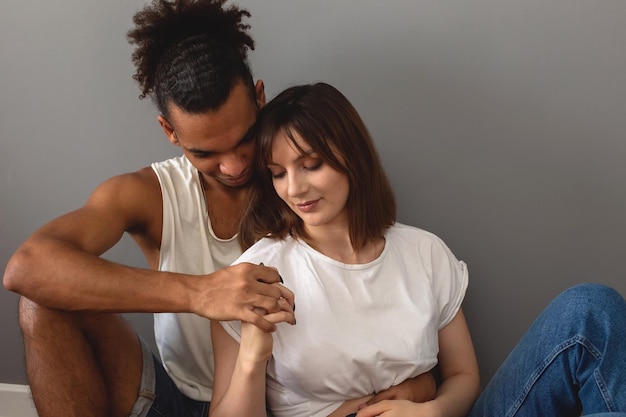 A couple a guy and a girl are sitting at home on the floor against a gray wall