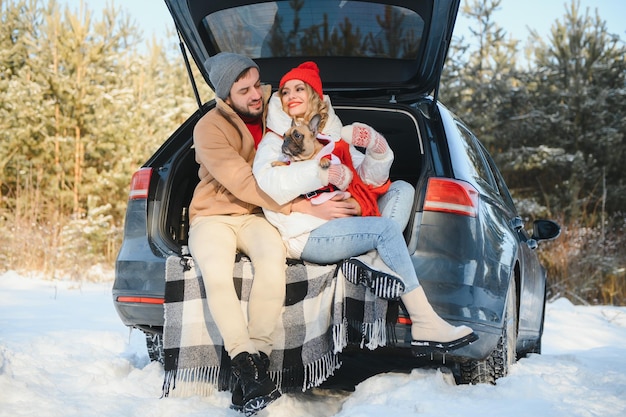 Couple guy and girl sitting in car playing with dog in winter forest