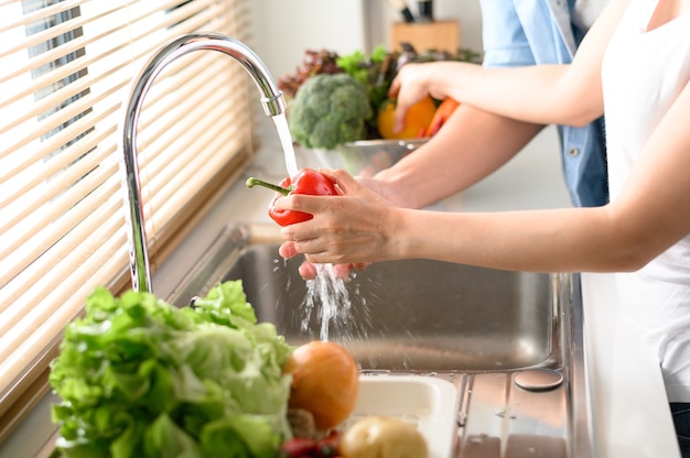 Coppia mano aiutandosi a vicenda per lavare il peperone rosso dolce fresco nel lavello della cucina